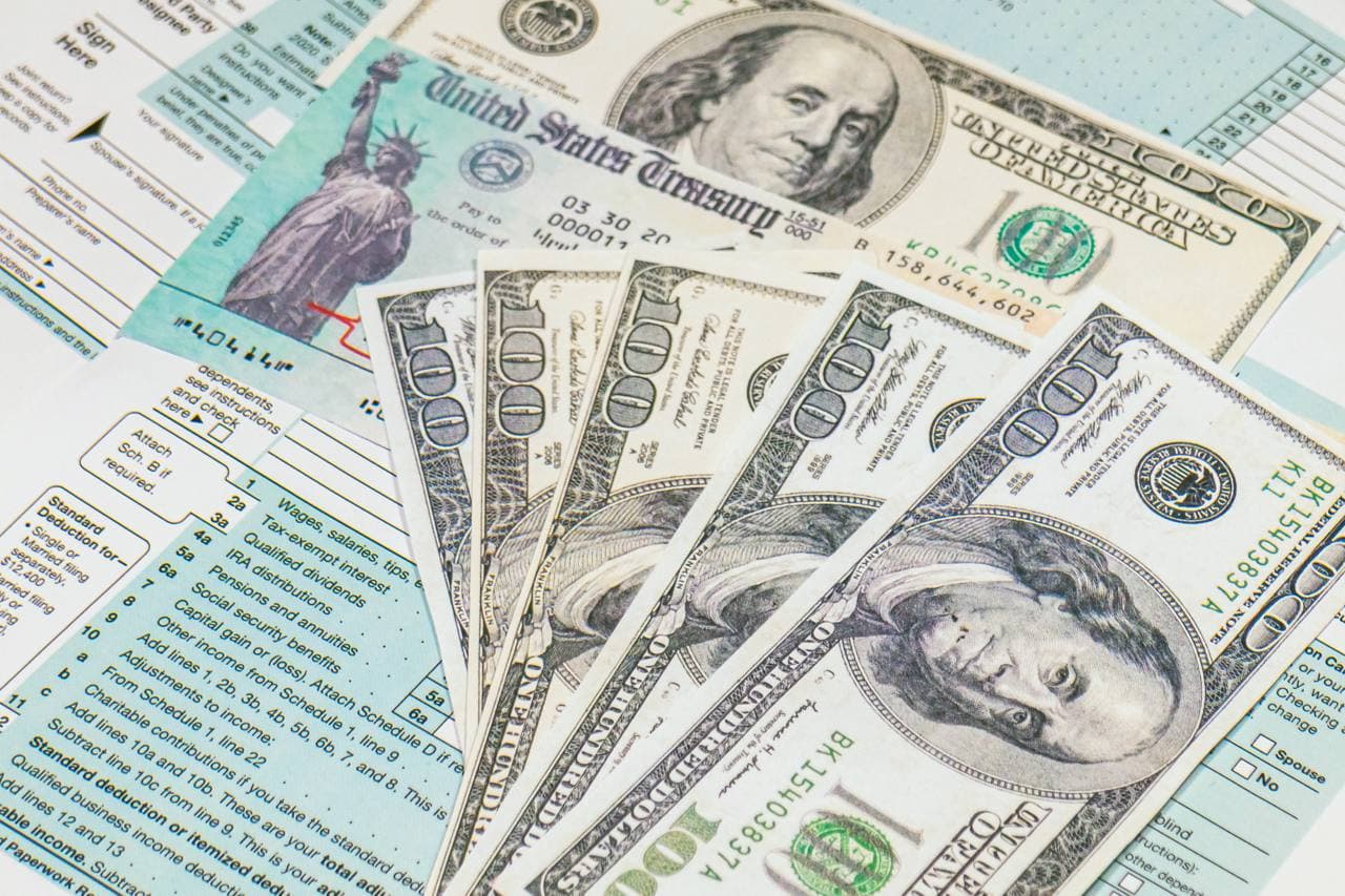 Tax forms, stimulus check, and cash representing an IRS refund